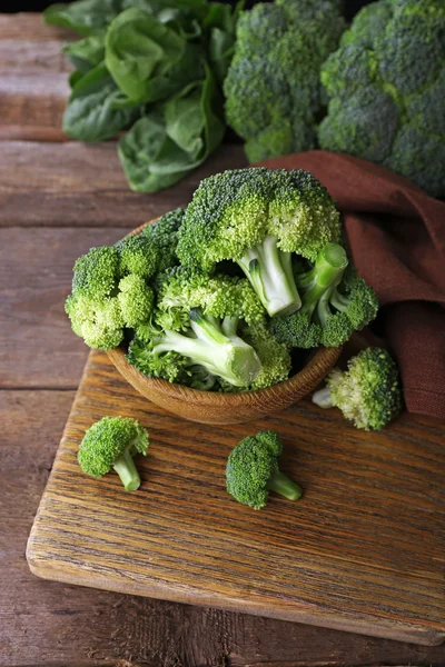 Čerstvé brokolice se špenátem v misce na dřevěný stůl zblízka — Stock fotografie