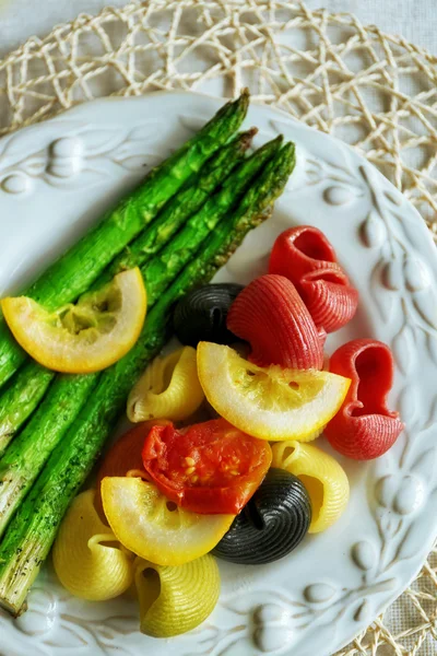 Rostad sparris och läckra färgglada pasta med grönsaker på tallriken på träbord bakgrund — Stockfoto