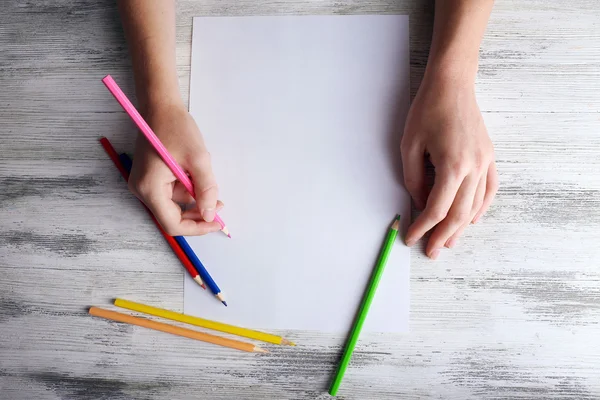 Hand met kleur potloden en blanco vel papier op houten tafel — Stockfoto