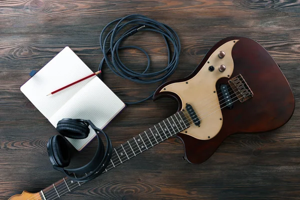 Electric guitar with headphones and notebook on wooden table close up — Stock Photo, Image