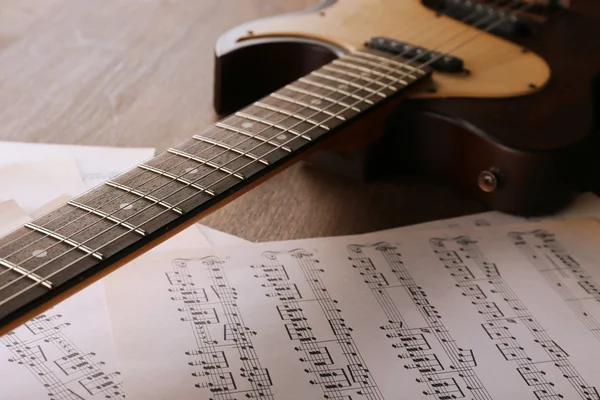 Chitarra elettrica con note musicali sul tavolo di legno da vicino — Foto Stock