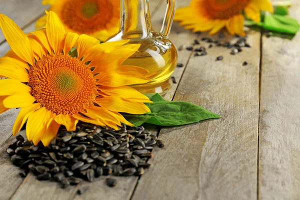 Beautiful bright sunflowers with seeds and bottle of oil on wooden table close up — Stock Photo, Image