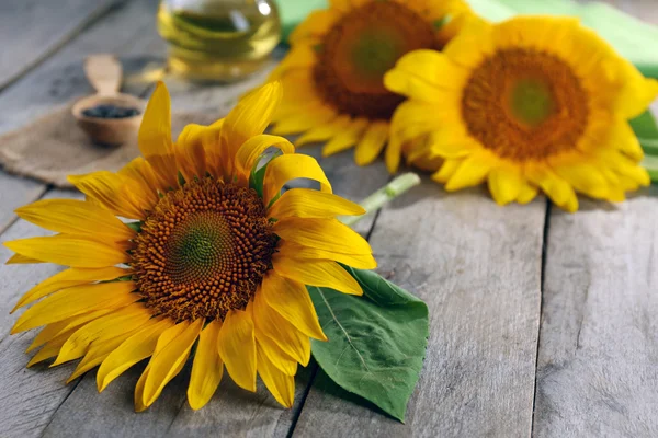 Beautiful bright sunflowers with bottle of oil on wooden table close up — Stock Photo, Image