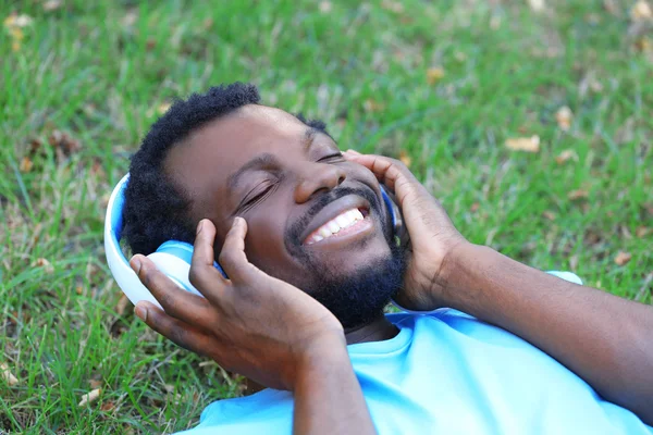 Hombre afroamericano con auriculares sobre hierba verde en el parque —  Fotos de Stock