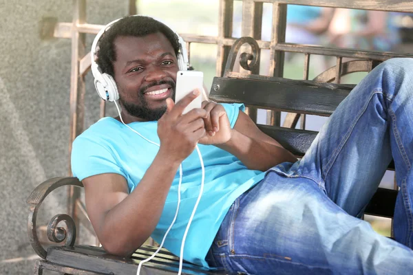 African American man with headphones on bench in park — Stock Photo, Image