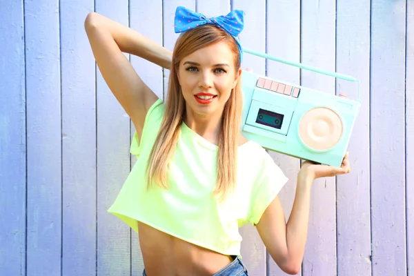 Beautiful girl with pretty smile holding retro tape recorder on color wooden background — Stock Photo, Image