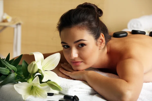 Jovem com pedras de spa em suas costas na mesa de massagem no salão de beleza spa — Fotografia de Stock