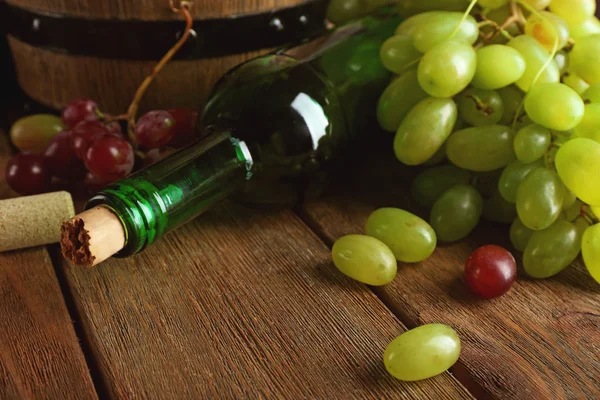 Bílé a červené hroznové v poli s láhví vína na dřevěné pozadí — Stock fotografie