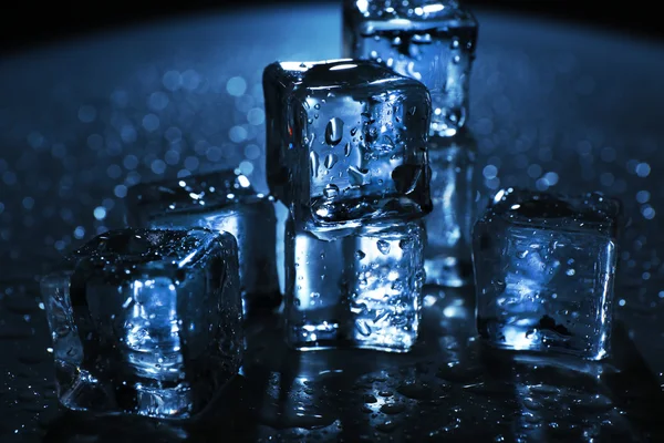 Melting ice cubes under blue light with drops around, close up