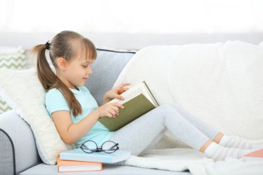 Kitap ile kanepede oturan küçük kız