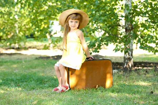 Niña con maleta en el césped en el parque —  Fotos de Stock