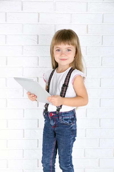 Liten flicka med tablett på tegel vägg bakgrund — Stockfoto