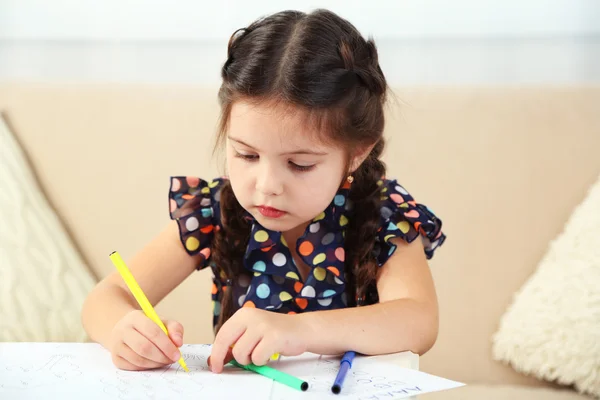 Милая маленькая девочка делает домашнее задание, крупным планом, на домашнем фоне интерьера — стоковое фото