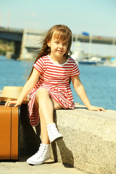 Kleines Mädchen mit Koffer am Flussufer — Stockfoto