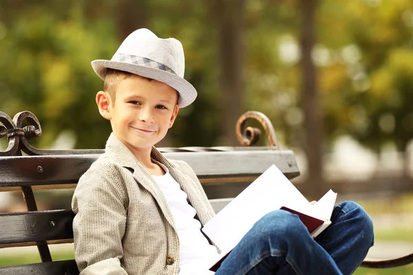 Bambino che legge libro su panchina nel parco — Foto Stock