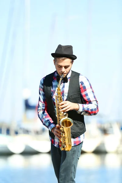 Jovem tocando saxofone na beira do rio — Fotografia de Stock