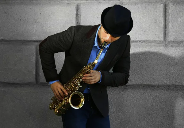 Hombre con saxofón afuera cerca de la pared de ladrillo — Foto de Stock