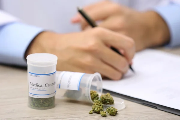 Médico escrevendo sobre prescrição em branco e garrafa com cannabis medicinal na mesa de perto — Fotografia de Stock