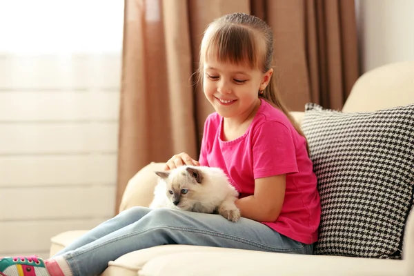 Girl playing with kitten on sofa — Stock Photo, Image