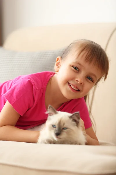 Girl playing with kitten on sofa — Stock Photo, Image