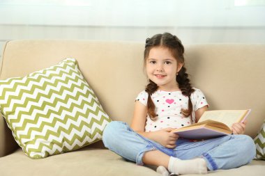 güzel küçük bir kız kanepe ile kitap, ev iç zemin üzerine oturan