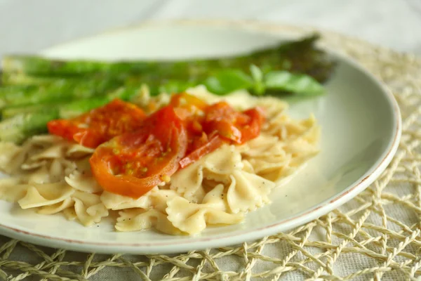 Roasted asparagus and tasty pasta with vegetables on plate on wooden table background — Stock Photo, Image