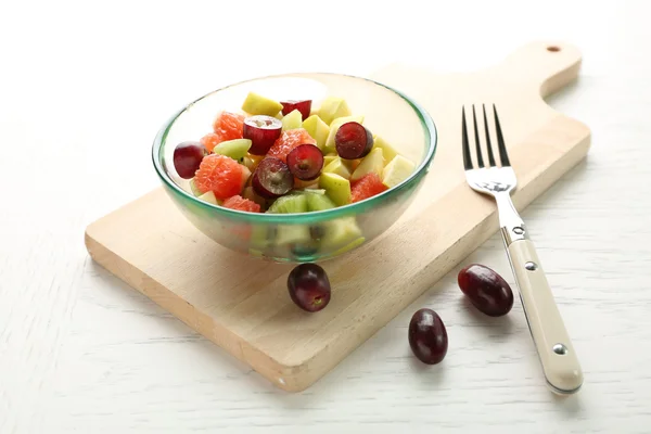 Insalata di frutta in ciotola di vetro, su fondo di legno chiaro — Foto Stock