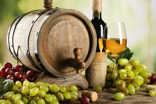 Uva blanca y roja con botella de vino cerca de barril en mesa de madera, de cerca —  Fotos de Stock