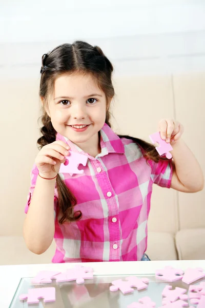 Cute little girl playing with puzzles on home interior background — Stock Photo, Image