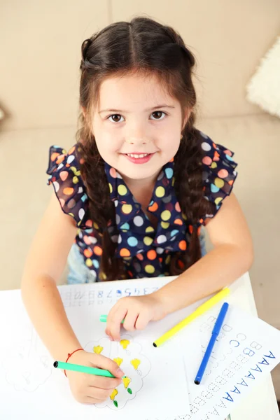 Carina bambina che fa i compiti, primo piano, su sfondo interno di casa — Foto Stock