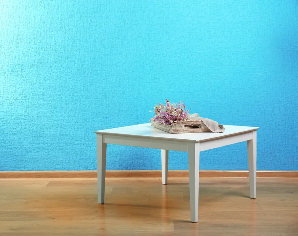 Pequeña mesa con flores sobre fondo de pared azul — Foto de Stock