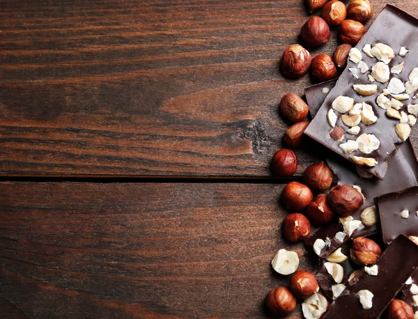 Pedaços de chocolate com nozes em fundo de madeira — Fotografia de Stock