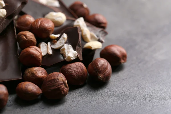 Части черного шоколада и орехи на темно-сером фоне — стоковое фото
