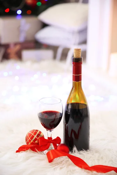 Bottiglia e bicchiere di vino con decorazioni natalizie contro le luci colorate bokeh sfondo — Foto Stock