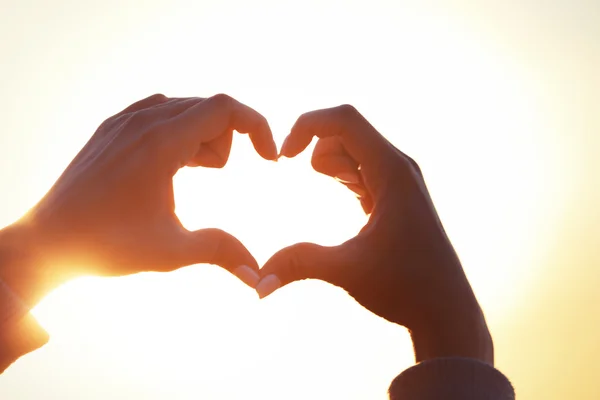 Handen in de vorm van liefde hart op zonlicht achtergrond — Stockfoto