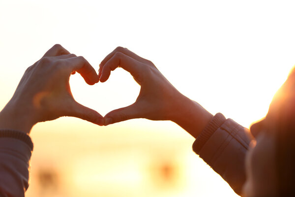 Hands in shape of love heart on sunlight background