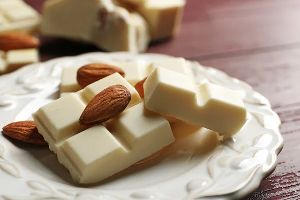 Части белого шоколада с орехами на тарелке, на фоне цвета дерева — стоковое фото