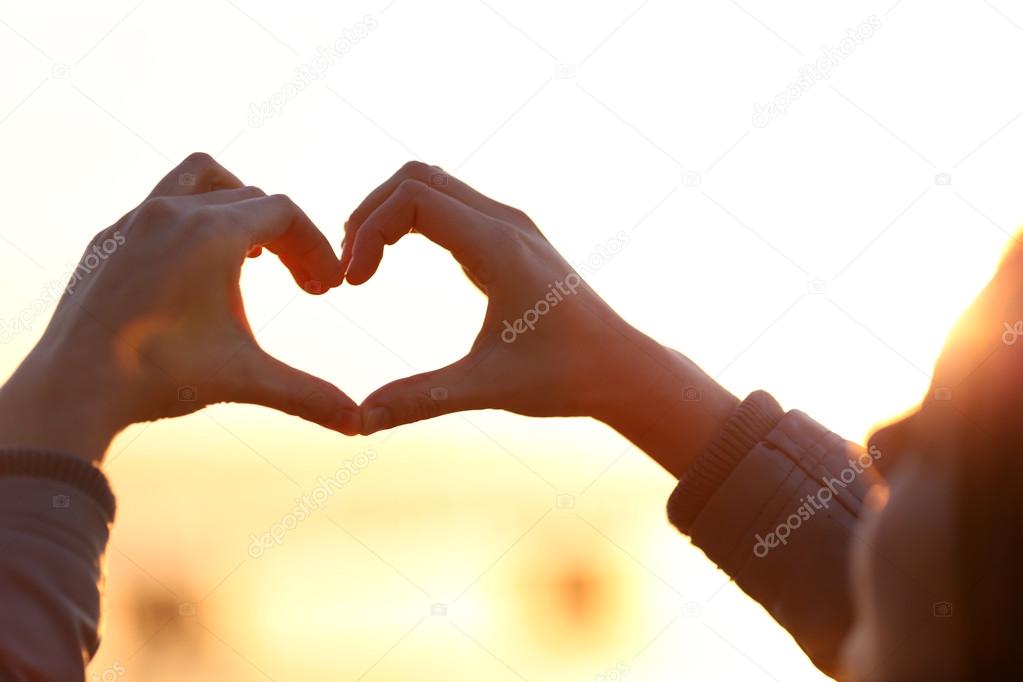 Hands in shape of love heart on sunlight background