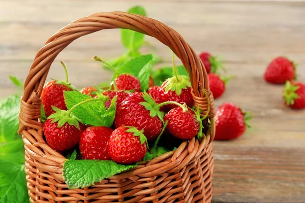 成熟的草莓在柳条篮子里的木桌前，特写 — 图库照片