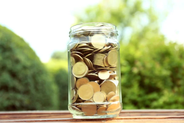 Monedas en frasco de dinero en la mesa al aire libre — Foto de Stock