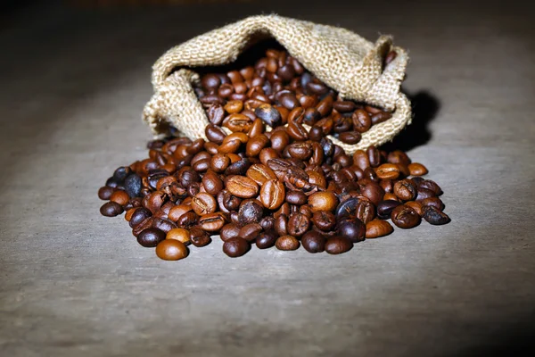 Coffee beans in sackcloth bag on wooden table — Stock Photo, Image