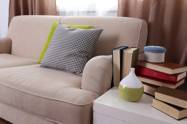 Canapé confortable avec oreillers et table avec livres près de lui dans la chambre, fermer — Photo