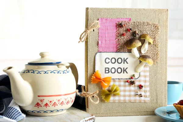 Libro de cocina decorado con tetera y sabroso pastel sobre fondo blanco — Foto de Stock