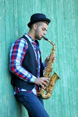 Genç adam eski duvarının yakınında dışında saksafon oynamaya