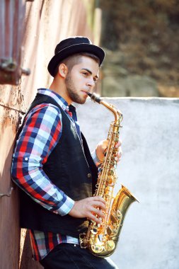 Genç adam eski duvarının yakınında dışında saksafon oynamaya