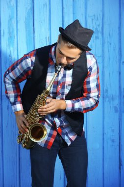 Yakışıklı adam şapkalı sax mavi ahşap arka plan üzerinde çalış.