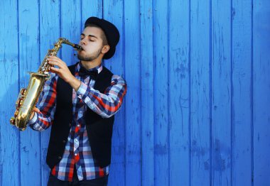 Yakışıklı adam şapkalı sax mavi ahşap arka plan üzerinde çalış.