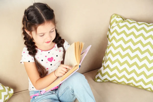 Bambina seduta sul divano con libro — Foto Stock