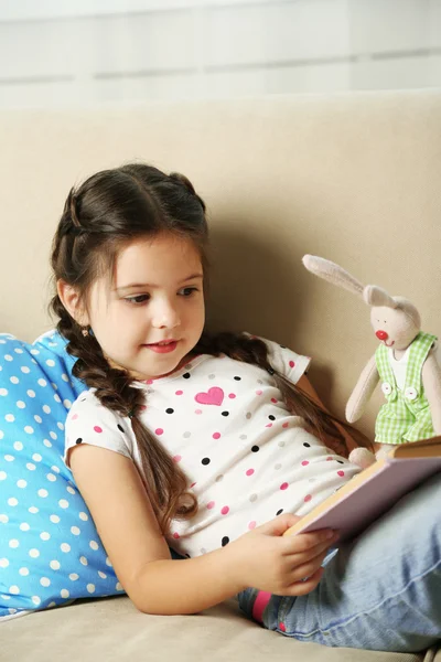 Petite fille assise sur un canapé avec un livre — Photo