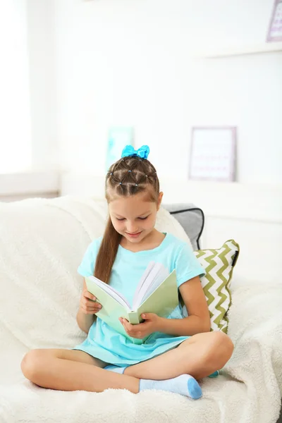 Menina sentada no sofá com livro — Fotografia de Stock